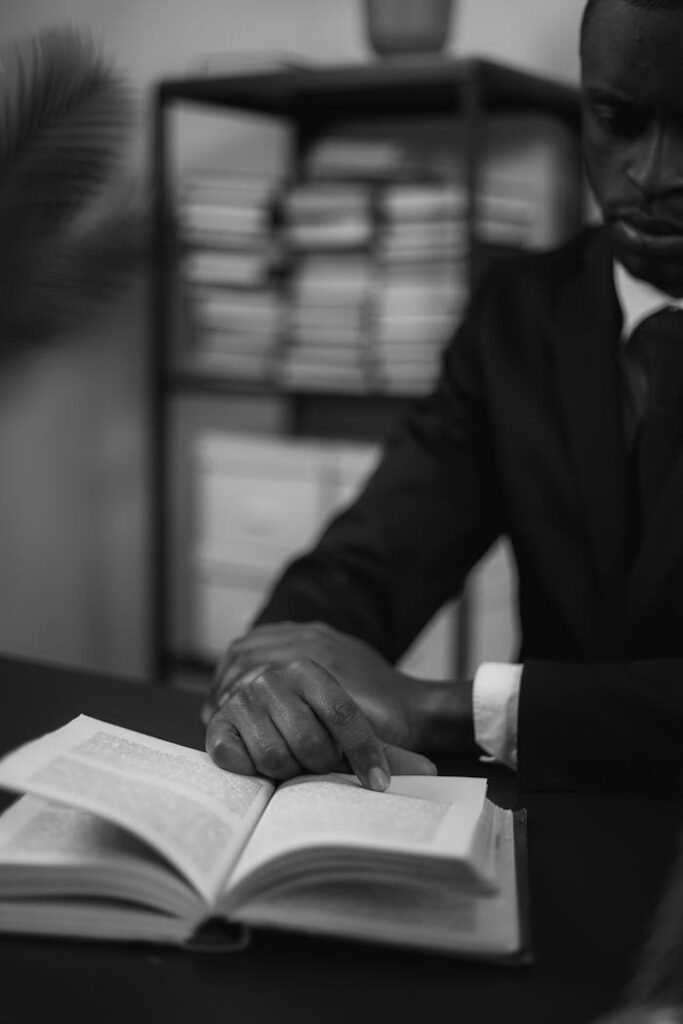 Black and white photo of a man in a suit reading a book in a corporate office setting.